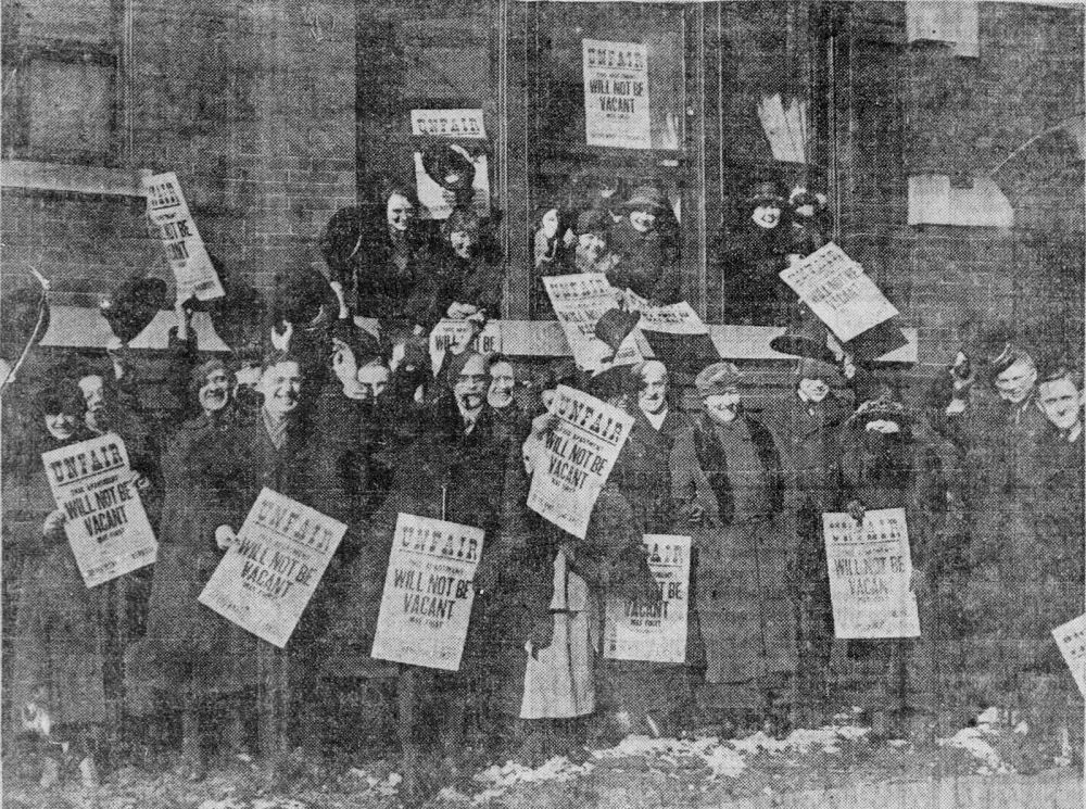 A vintage black-and-white photo of a large group holding protest signs outside a building.