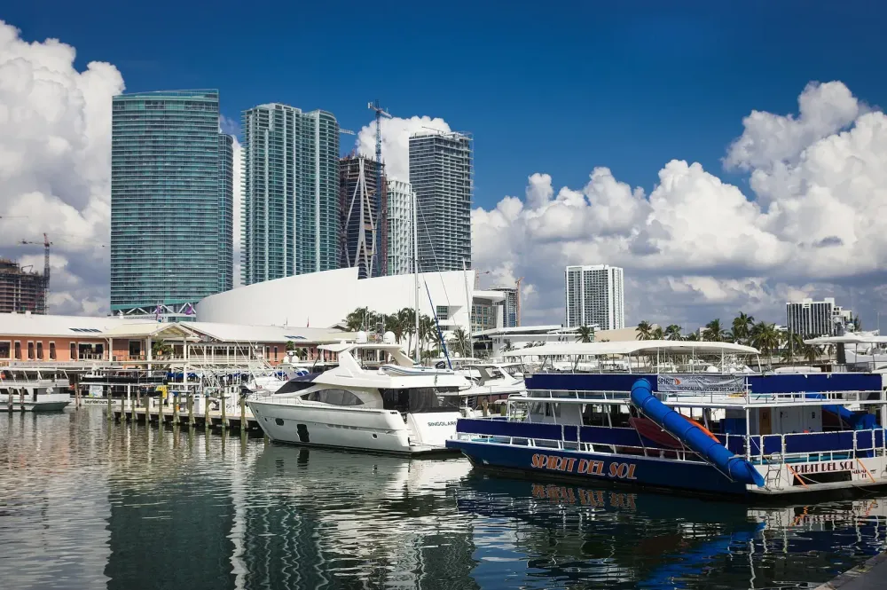 Yachten und Boote im Jachthafen vor einer modernen Skyline mit Wolkenkratzern.