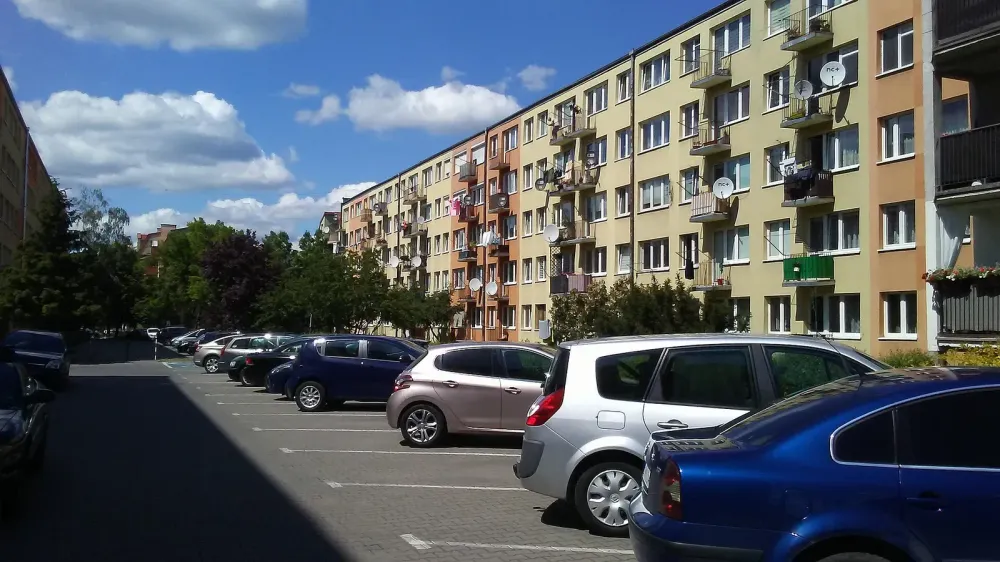 A row of apartment buildings in Europe next to a parking lot with cars.