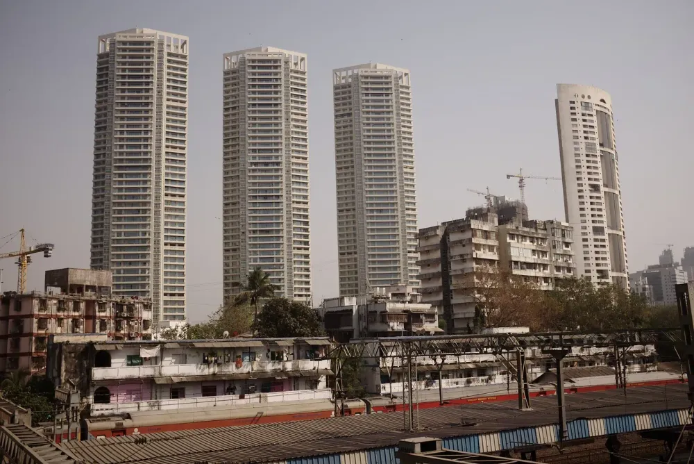 Modern high-rise towers rising behind older low-rise buildings and a railway station in Mumbai.