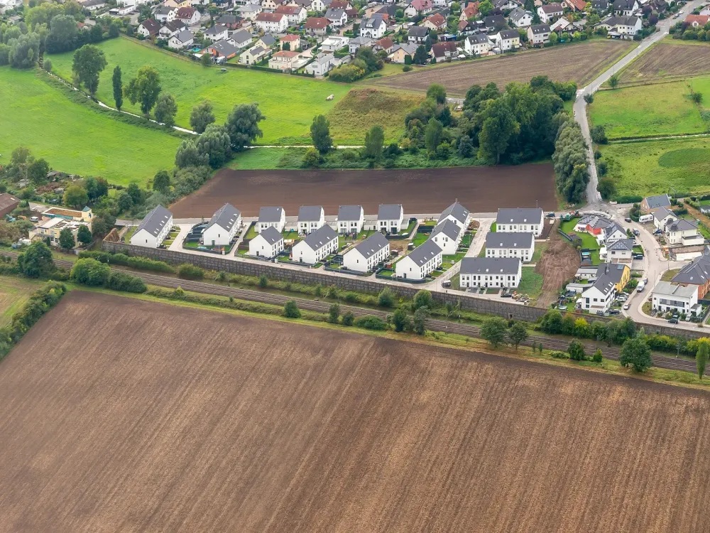 Aerial view of a new residential development with white houses and dark roofs next to fields and train tracks.