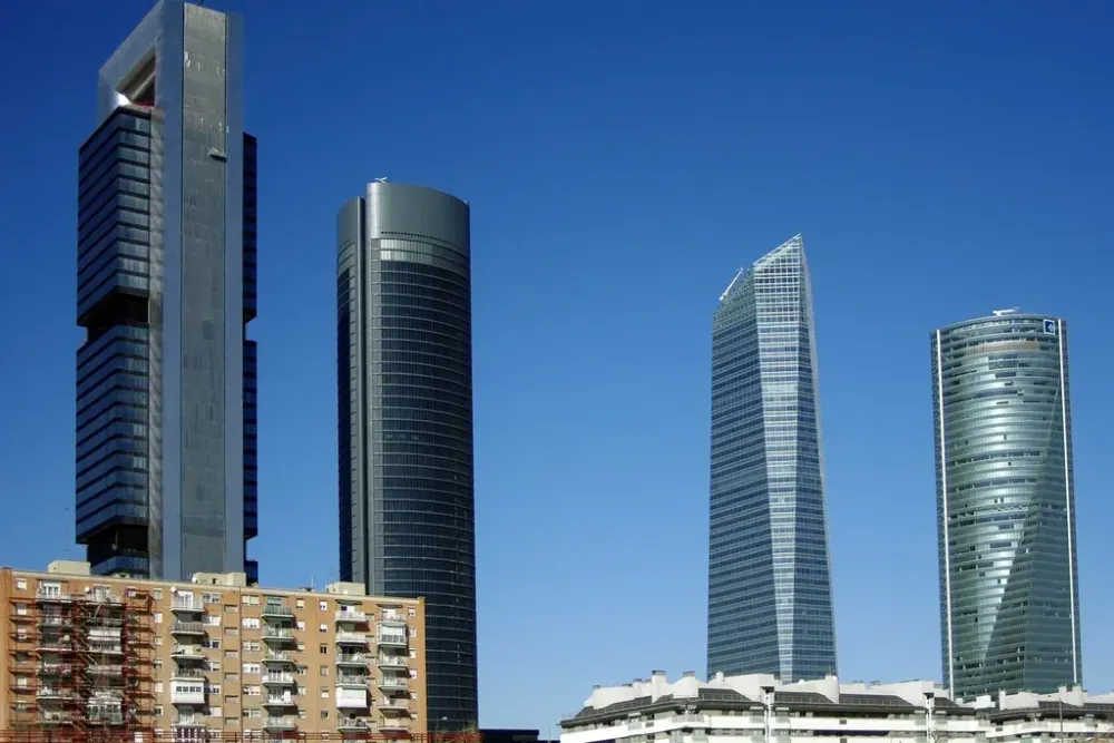 Modern skyscrapers and a residential apartment building under a clear blue sky in Madrid, Spain.