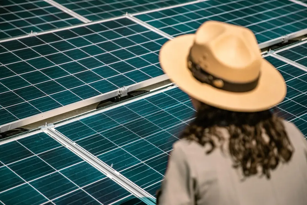 Rückansicht einer Frau mit breitkrempigem Hut vor einer Solarmodul-Anlage.