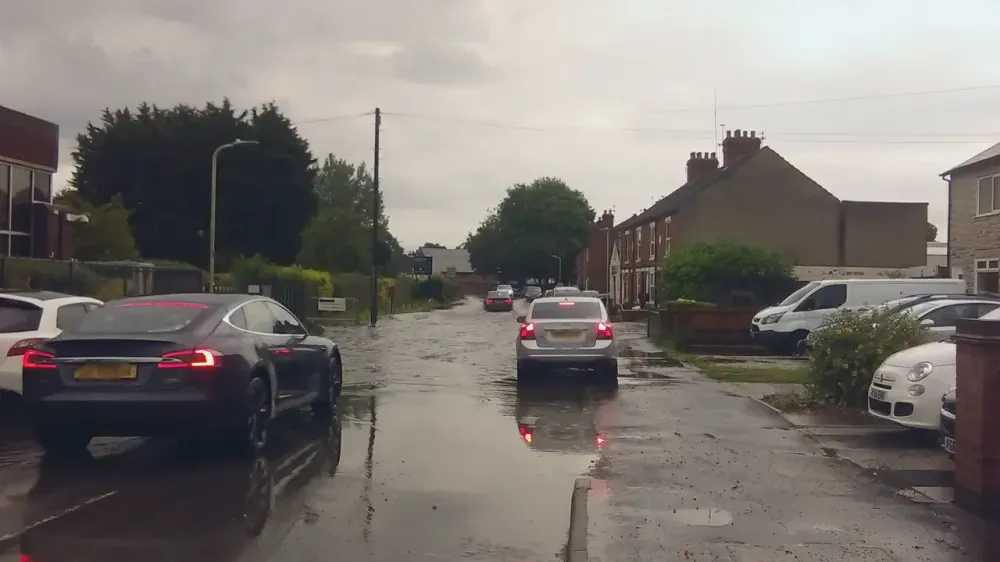 Cars drive through deep floodwater on a residential street in England.