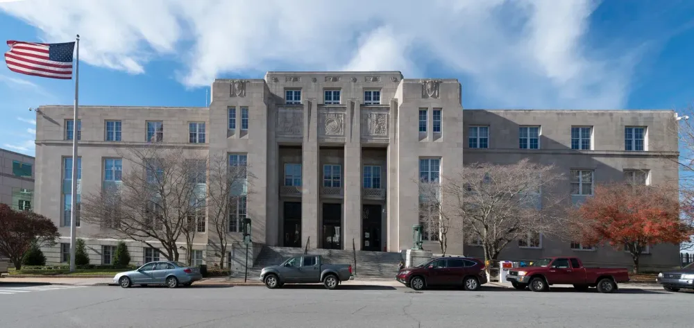 Large Art Deco stone government building with a US flag and parked cars under a blue sky.